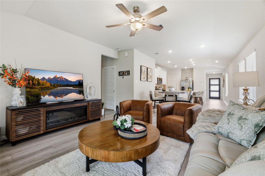 Modern open-concept living area with a cozy seating arrangement, featuring leather chairs and a plush sofa. The space is well-lit with natural light from multiple windows and a ceiling fan.