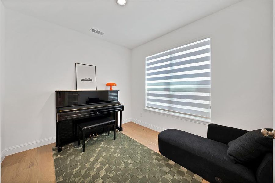 Bright interior space featuring a large window with horizontal blinds, light wood-finish flooring, and white baseboards