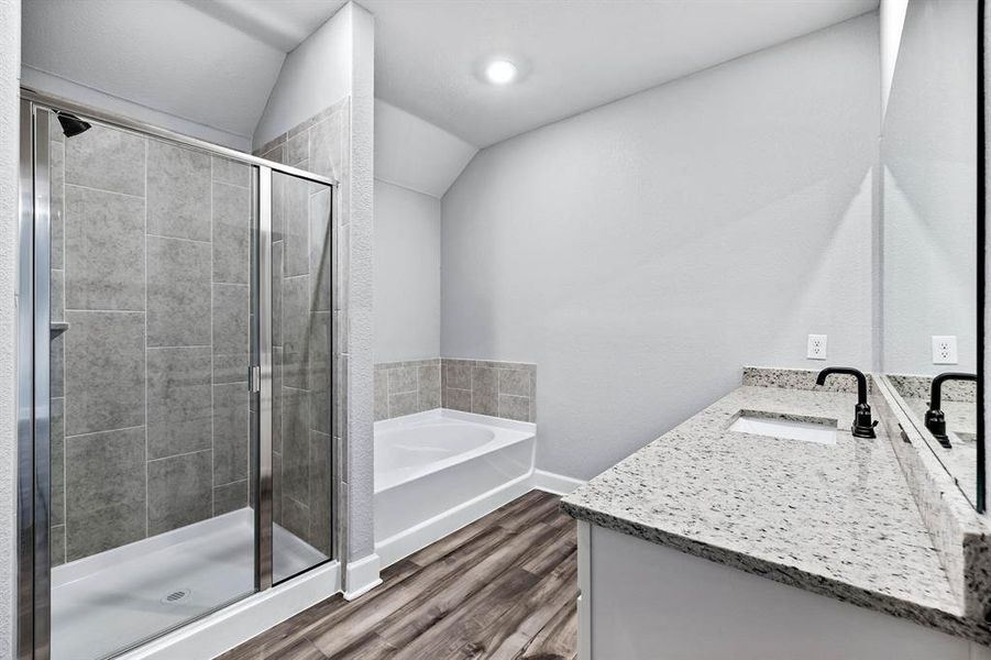 Bathroom with lofted ceiling, wood finished floors, vanity, a bath, and a stall shower