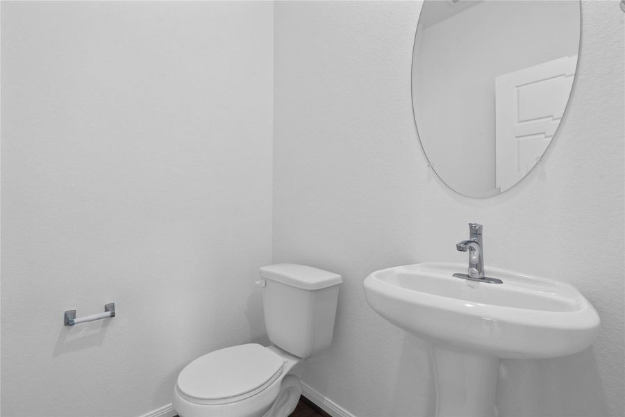 The powder room on the first floor includes a pedestal sink, oval mirror, and toilet to conveniently meet your needs.