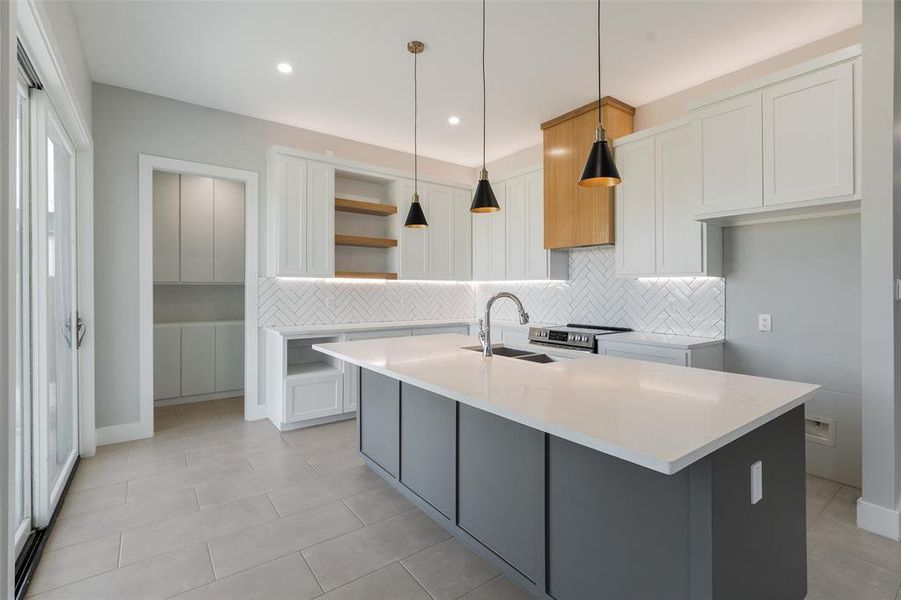 Kitchen featuring hanging light fixtures, white cabinets, backsplash, a kitchen island with sink, and sink