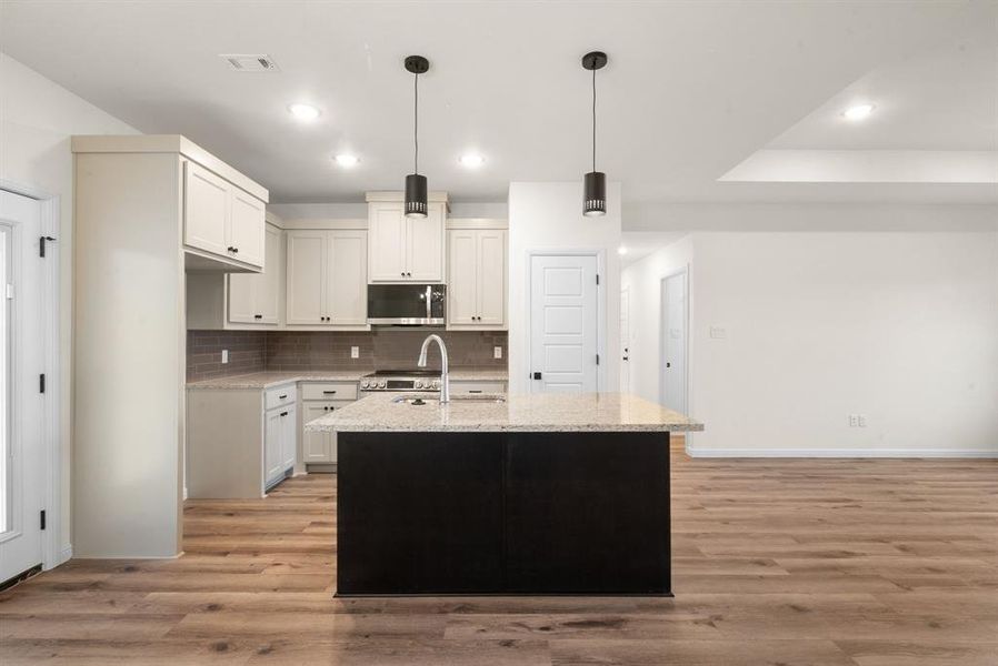 Kitchen featuring light stone countertops, hanging light fixtures, a kitchen island with sink, white cabinets, and appliances with stainless steel finishes Kitchen featuring light stone countertops, hanging light fixtures, a kitchen island with sink, white cabinets, and appliances with stainless steel finishes