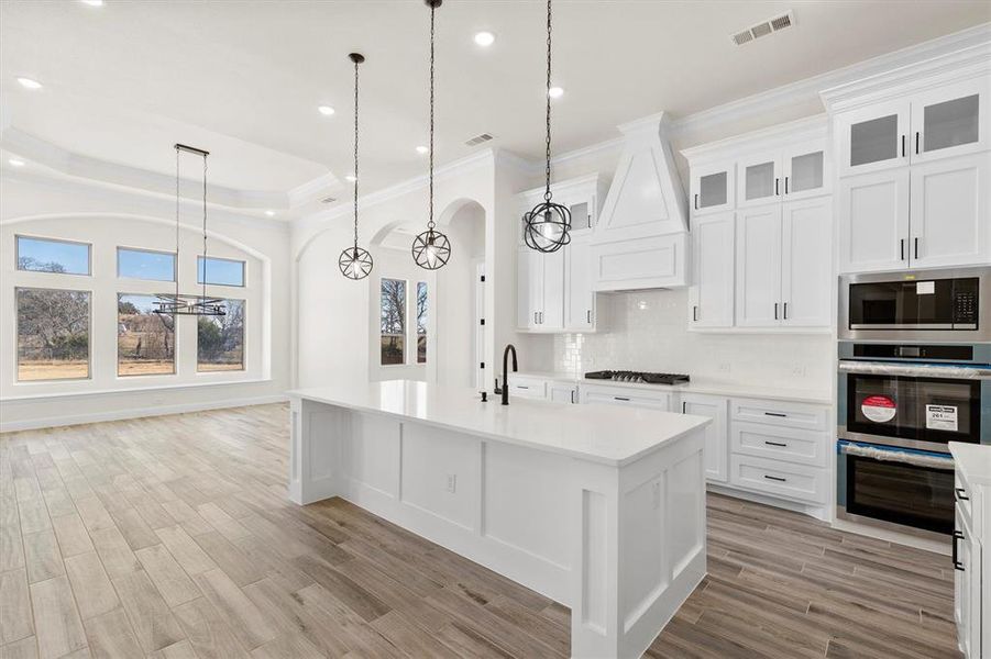 Kitchen featuring an island with sink, white cabinetry, pendant lighting, and appliances with stainless steel finishes