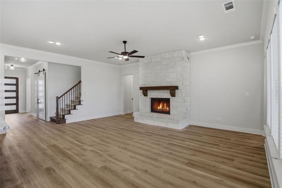 Unfurnished living room with a barn door, ceiling fan, light wood finished floors, a fireplace, and crown molding