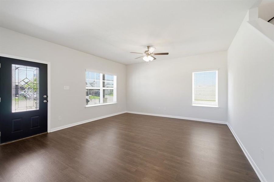 Bright living area featuring wood-finish flooring, a decorative front door with leaded glass, multiple windows with blinds, a ceiling fan with light fixture, and neutral wall tones