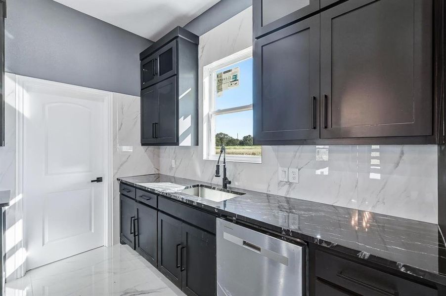 Kitchen featuring dark stone counters, backsplash, glass insert cabinets, and stainless steel dishwasher