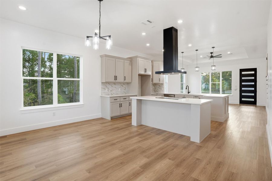 Kitchen featuring a center island, range hood, light wood-type flooring, backsplash, and a chandelier