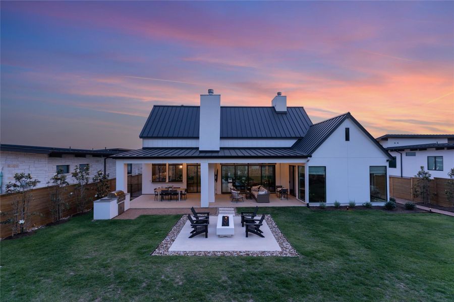 Expansive backyard featuring a manicured lawn, covered patio, outdoor kitchen, and a fire pit area with seating Expansive backyard featuring a manicured lawn, covered patio, outdoor kitchen, and a fire pit area with seating