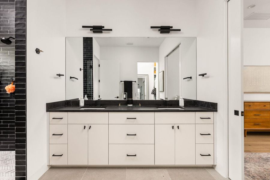 A well-appointed primary bathroom features a long dual vanity with black countertops and sleek fixtures. A well-appointed primary bathroom features a long dual vanity with black countertops and sleek fixtures.