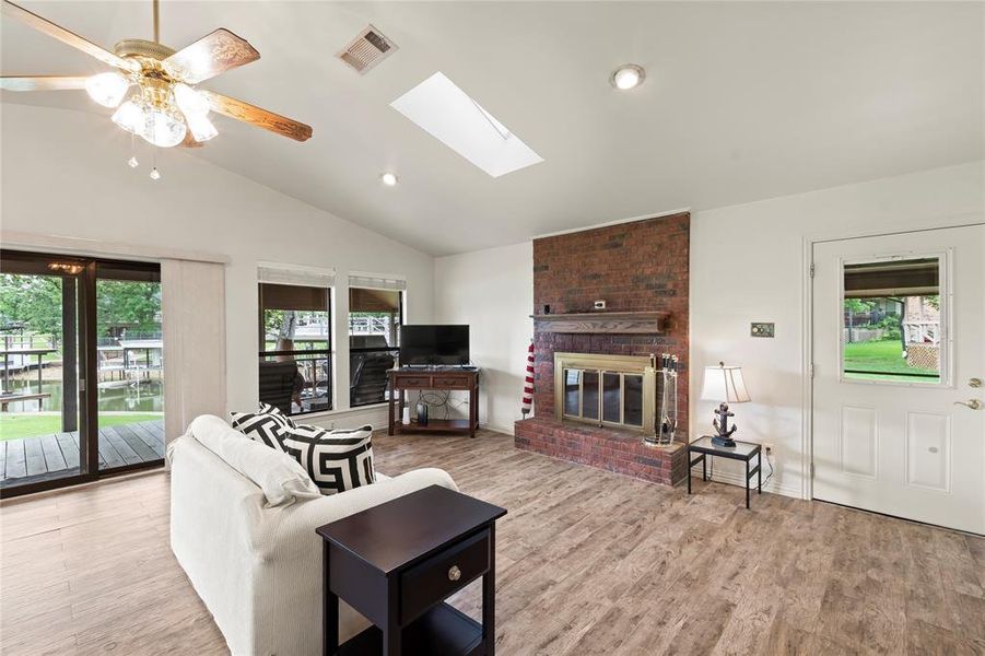 Bright and airy living room with open floor plan, wood-grain porcelain tile, and large windows bringing in natural light and lake views.