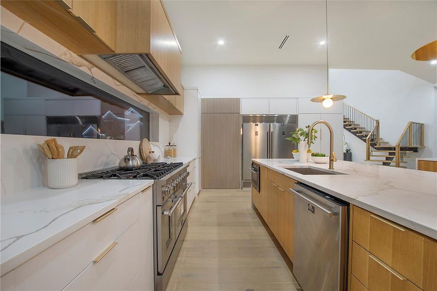 Kitchen featuring light stone countertops, sink, decorative light fixtures, and premium appliances