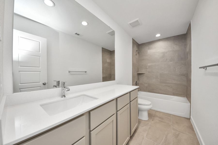 Secondary bath features tile flooring, bath/shower combo with tile surround, light stained wood cabinets, beautiful light countertop. Sample photo of completed home with similar floor plan. Actual colors and selections may vary.