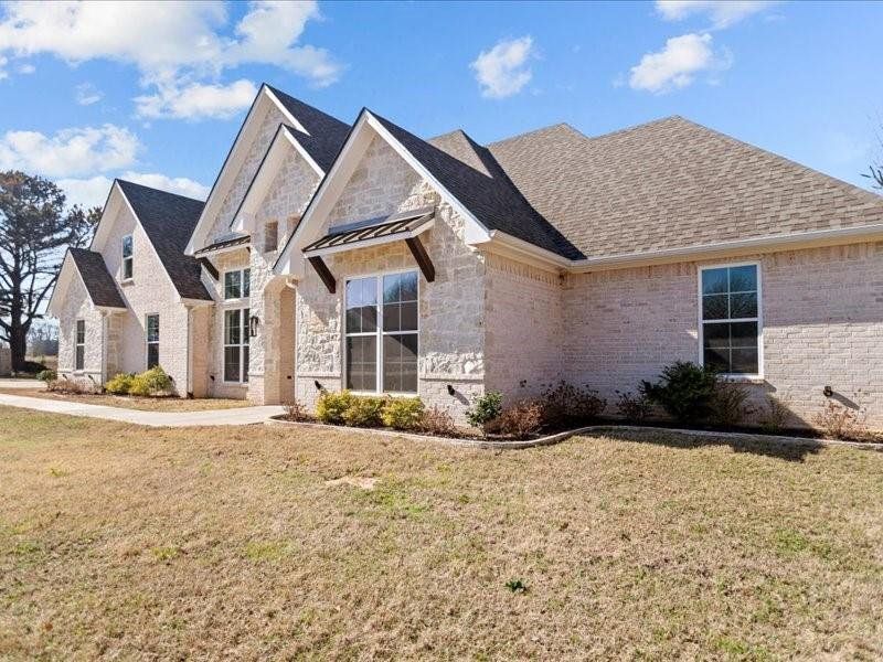 French provincial home featuring stone siding, brick siding, a front yard, and a shingled roof