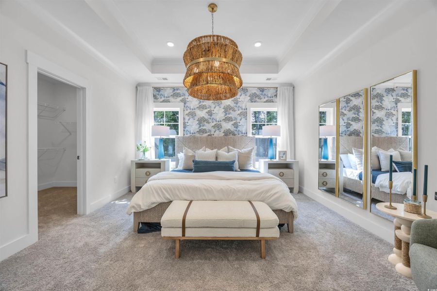 Carpeted bedroom with a tray ceiling, a spacious closet, a chandelier, and recessed lighting