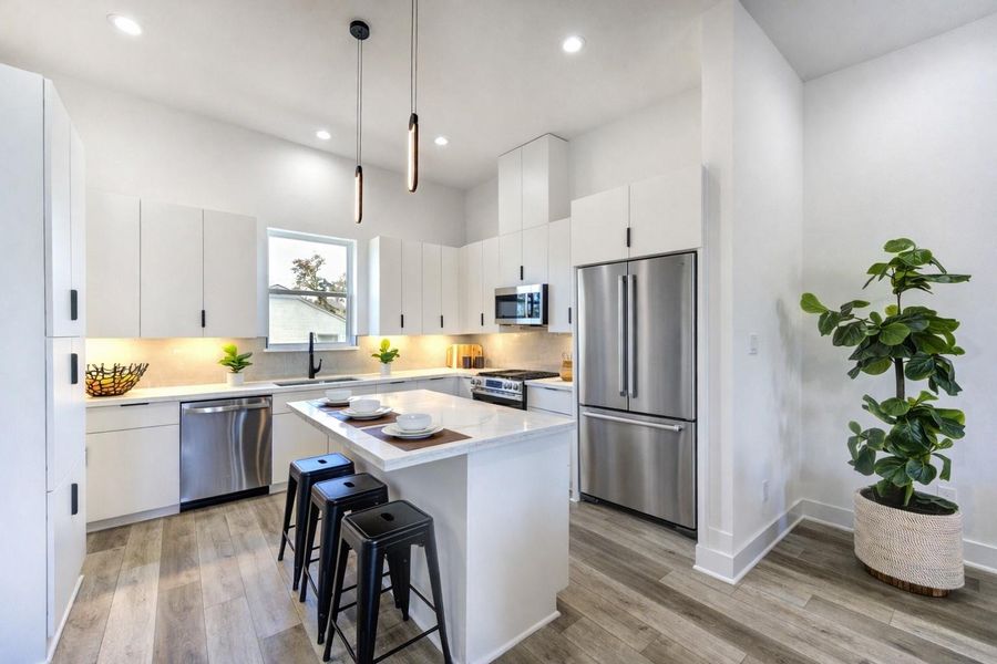 This modern kitchen features sleek white cabinetry, stainless steel appliances, and a spacious island with pendant lighting.