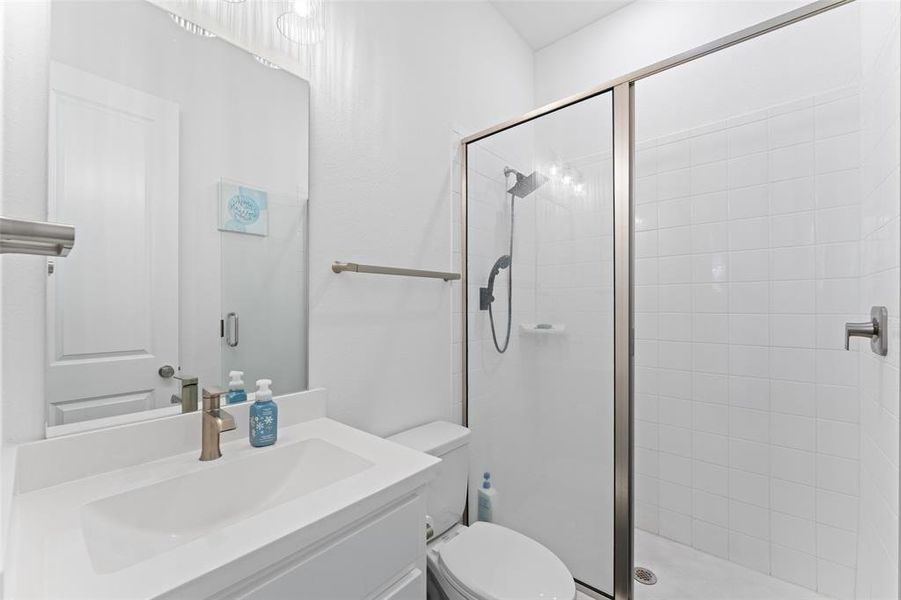 Bathroom featuring a vanity with an integrated sink, a large mirror, a toilet, and a glass-enclosed shower with a tiled surround