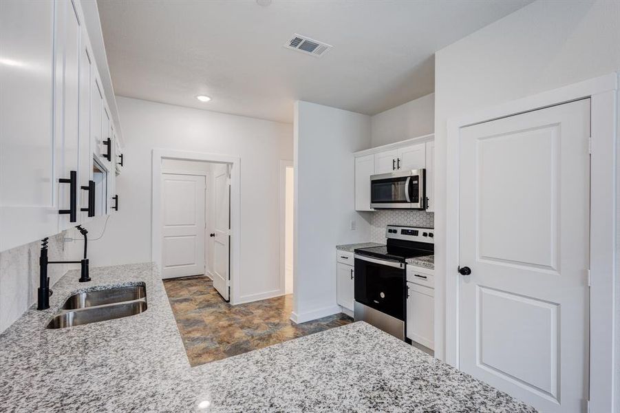 Kitchen with stainless steel appliances, decorative backsplash, white cabinets, light stone counters, and light tile patterned floors