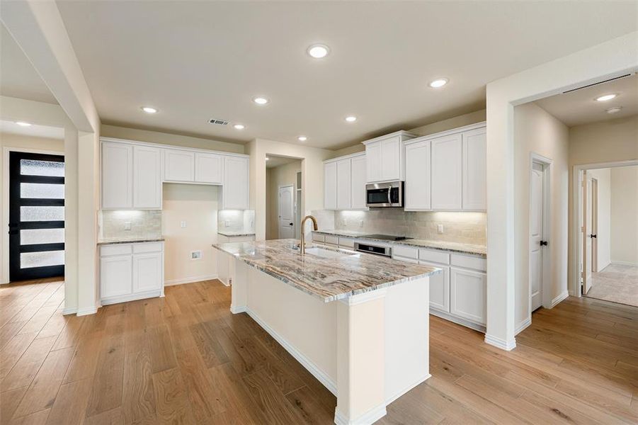 Kitchen with white cabinets, light stone countertops, light wood-type flooring, stainless steel microwave, and a kitchen island with sink