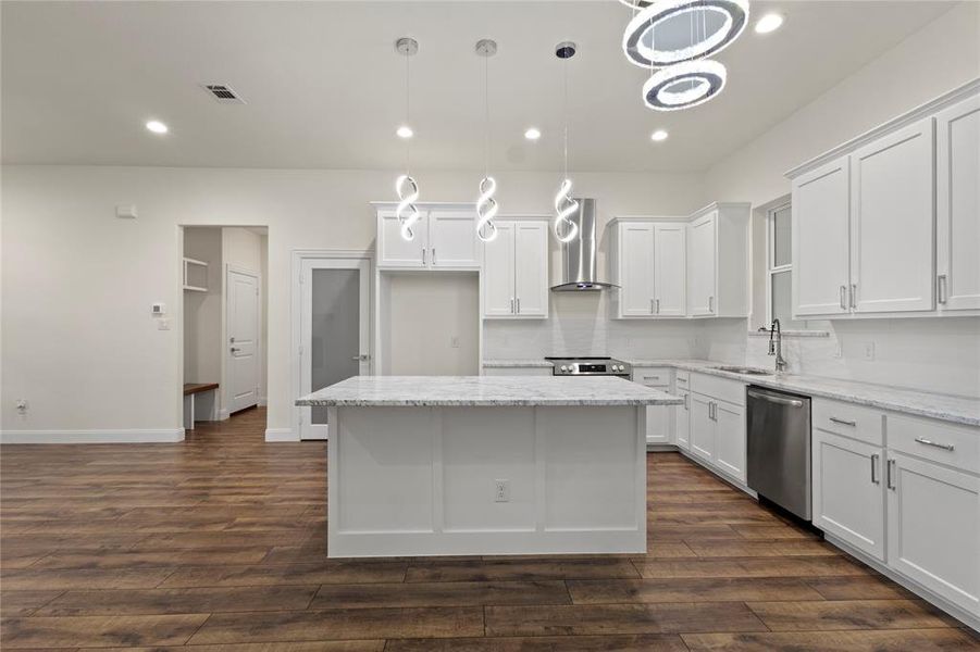 Contemporary kitchen featuring a large central island with a light-toned countertop, white cabinetry, stainless steel appliances, and wood-finish flooring Contemporary kitchen featuring a large central island with a light-toned countertop, white cabinetry, stainless steel appliances, and wood-finish flooring
