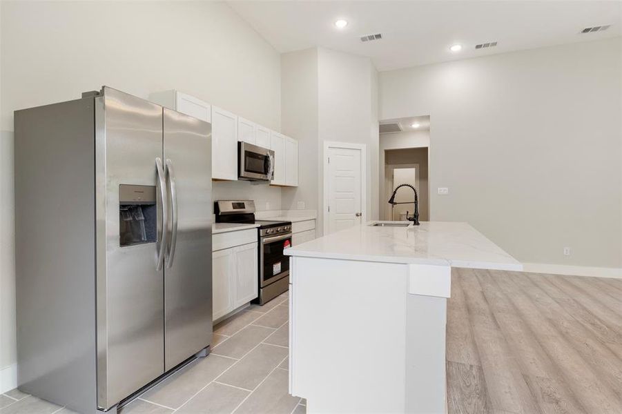 Kitchen with white cabinetry, light wood-type flooring, stainless steel appliances, a kitchen island with sink, and sink