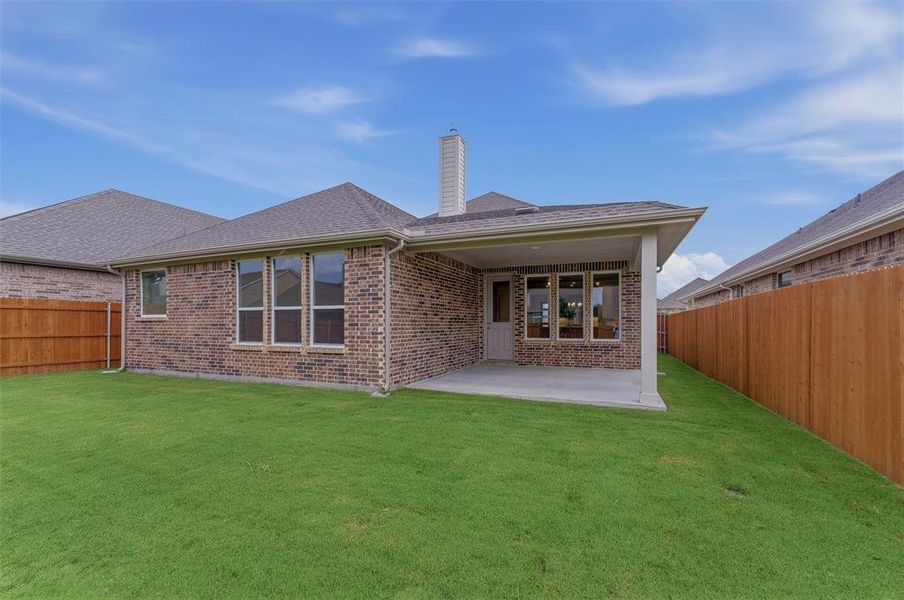 Expansive green lawn with a covered patio, brick exterior, and a privacy fence