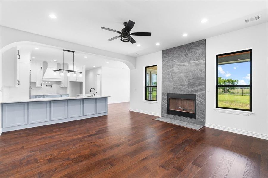 Unfurnished living room with dark wood-style flooring, recessed lighting, arched walkways, ceiling fan, and a fireplace Unfurnished living room with dark wood-style flooring, recessed lighting, arched walkways, ceiling fan, and a fireplace