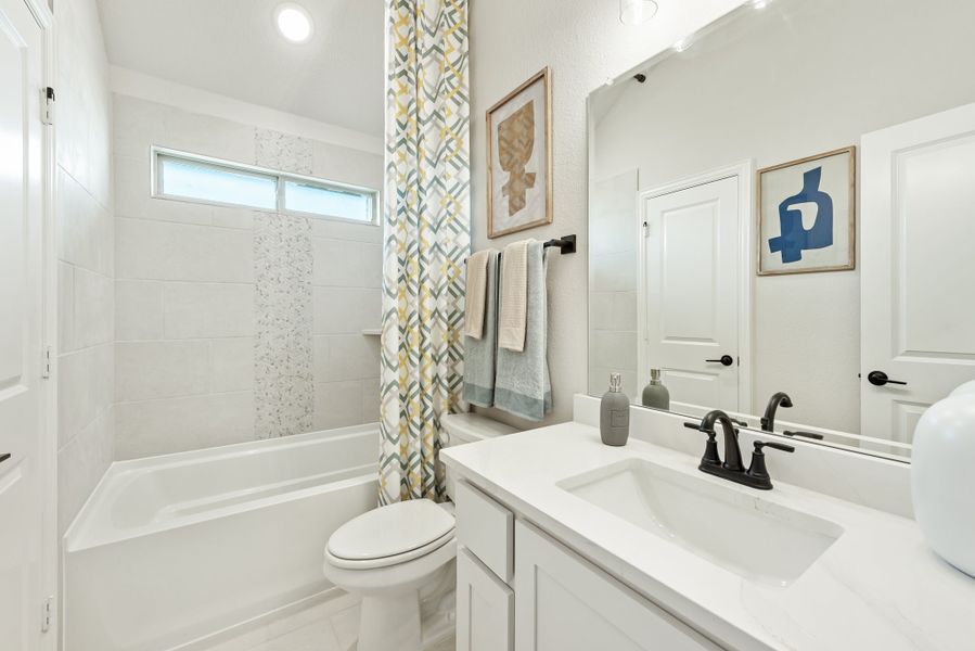 Bathroom with white vanity, tub-shower combo with patterned curtain, and tiled walls