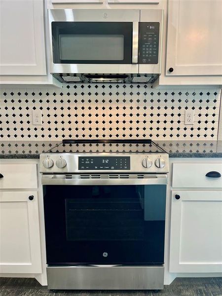 Kitchen featuring decorative backsplash, white cabinets, stainless steel appliances, and dark stone countertops