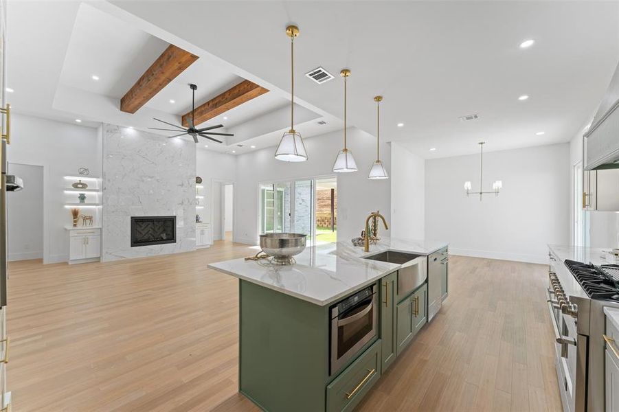 Kitchen featuring green cabinetry, ceiling fan, hanging light fixtures, light stone counters, and a center island with sink