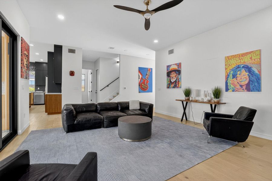 Living area with light wood-style flooring, ceiling fan, recessed lighting, and stairs
