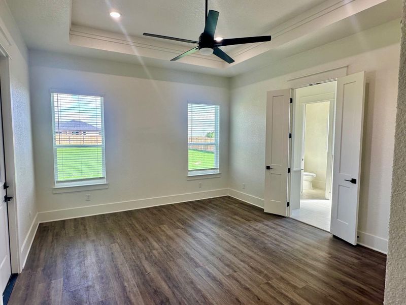 Unfurnished bedroom featuring dark wood finished floors, a tray ceiling, a ceiling fan, a textured wall, and ornamental molding