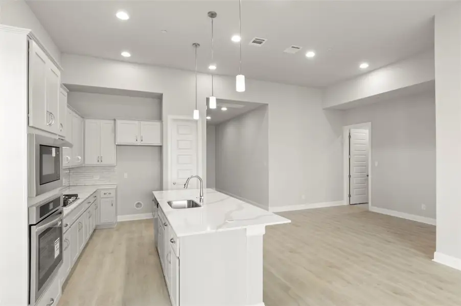 Kitchen with light wood-type flooring, stainless steel oven, a center island with sink, tasteful backsplash, and light stone countertops Kitchen with light wood-type flooring, stainless steel oven, a center island with sink, tasteful backsplash, and light stone countertops