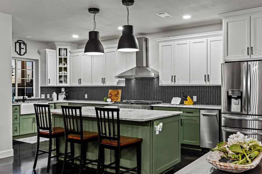 Kitchen featuring green cabinetry, backsplash, a kitchen breakfast bar, stainless steel refrigerator with ice dispenser, and light stone counters Kitchen featuring green cabinetry, backsplash, a kitchen breakfast bar, stainless steel refrigerator with ice dispenser, and light stone counters
