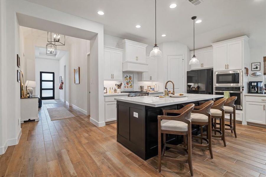 Kitchen featuring light wood-style flooring, light countertops, a breakfast bar, appliances with stainless steel finishes, and white cabinetry Kitchen featuring light wood-style flooring, light countertops, a breakfast bar, appliances with stainless steel finishes, and white cabinetry