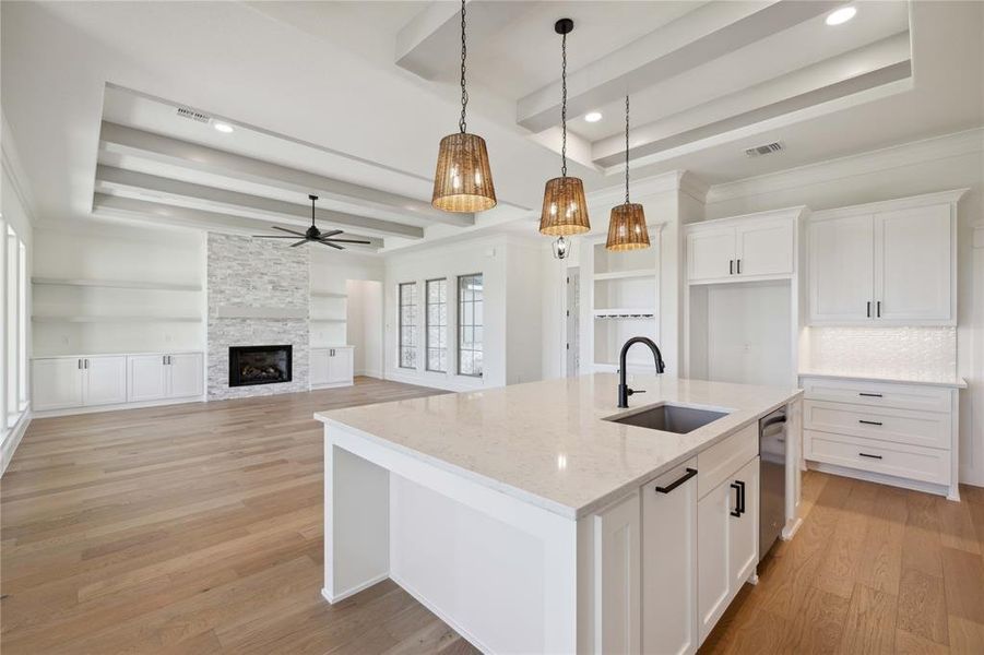 Kitchen featuring a raised ceiling, light stone counters, sink, and white cabinetry