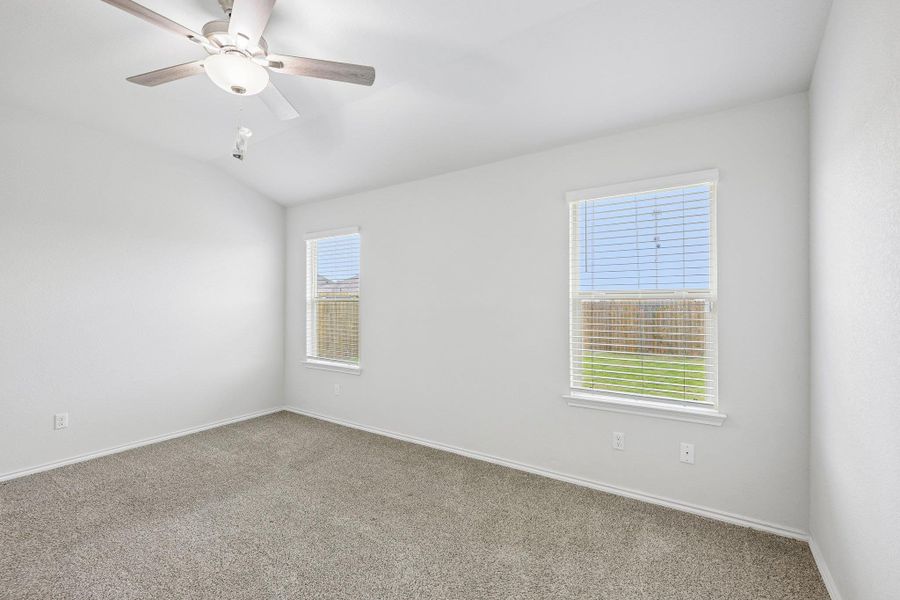 Spacious room featuring vaulted ceilings, a ceiling fan with light fixture, gray carpeting, and two windows with blinds