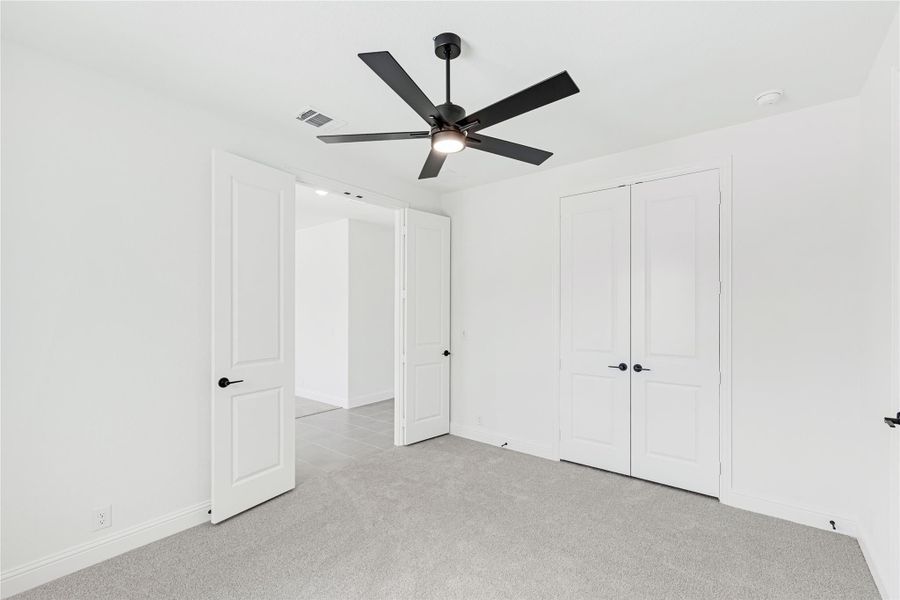 Empty bedroom with gray carpet, black ceiling fan, and white double closet doors