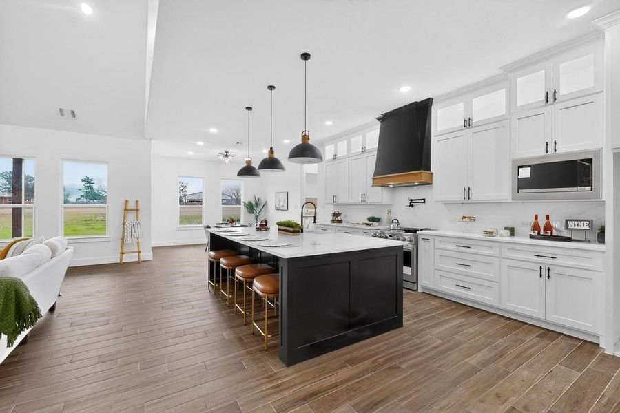 Kitchen with white cabinets, a kitchen breakfast bar, glass insert cabinets, hanging light fixtures, and a large island with sink Kitchen with white cabinets, a kitchen breakfast bar, glass insert cabinets, hanging light fixtures, and a large island with sink