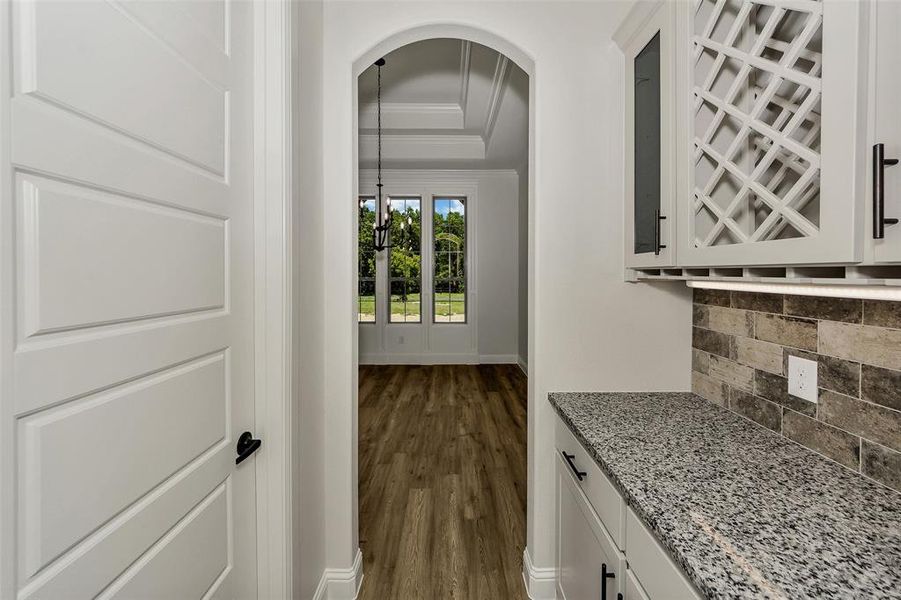 Bar area with crown molding, backsplash, arched walkways, dark wood-type flooring, and a raised ceiling