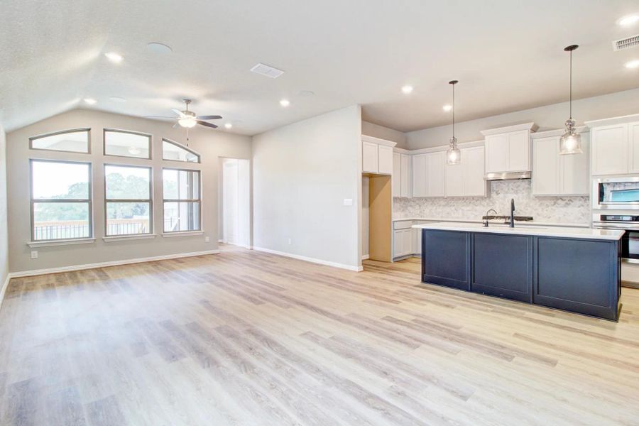 Kitchen featuring white cabinetry, decorative light fixtures, backsplash, stainless steel appliances, and light wood-style flooring Kitchen featuring white cabinetry, decorative light fixtures, backsplash, stainless steel appliances, and light wood-style flooring