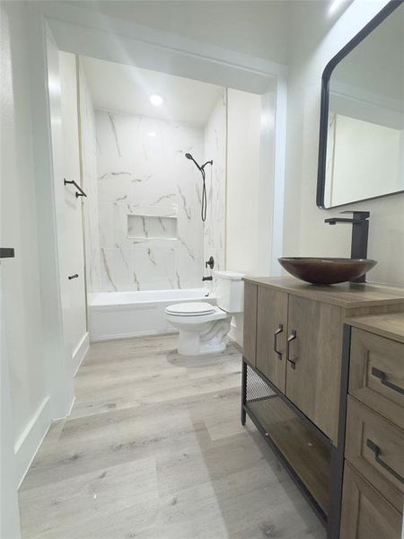 Full bathroom with wood-type flooring, toilet, vanity, and tiled shower / bath