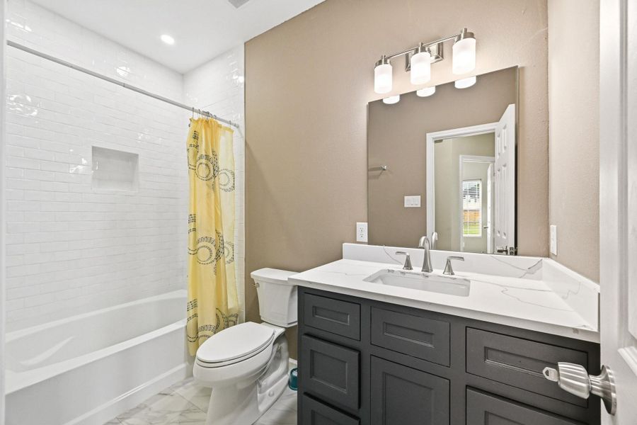 This stylish bathroom features a modern design with sleek finishes and a bright, clean aesthetic throughout. The dark vanity cabinetry pairs beautifully with the quartz-style countertop, creating a sophisticated contrast complemented by contemporary fixtures and lighting. The tub and shower combination is surrounded by elegant white subway tile extending to the ceiling, adding both texture and timeless appeal.
