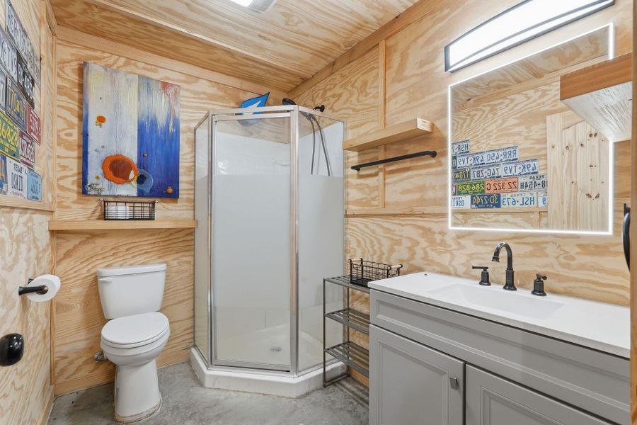 This bathroom features a modern, rustic design with plywood walls, a sleek corner shower, and a stylish vanity in the shop area.