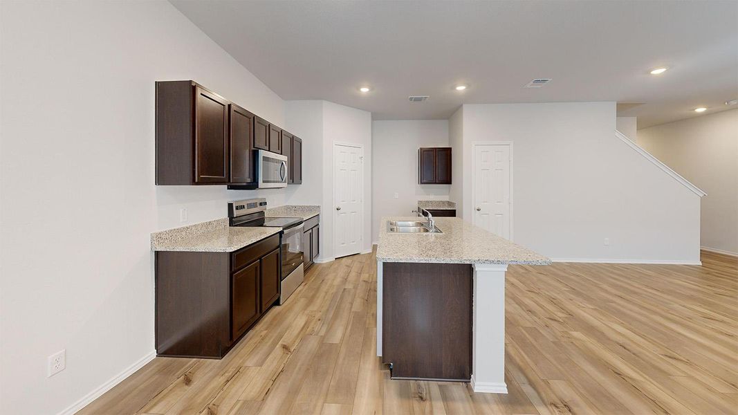 Kitchen with dark wood finish cabinetry, stainless steel appliances, light wood-type flooring, recessed lighting, and light stone countertops