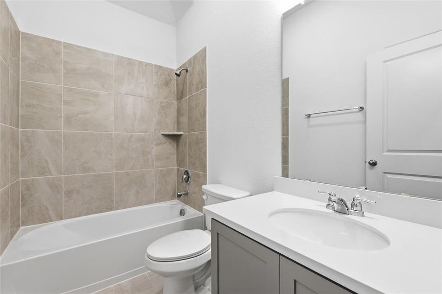 Bathroom featuring a white bathtub, ceramic tile surround with built-in shelf, gray vanity with white countertop, and chrome fixtures