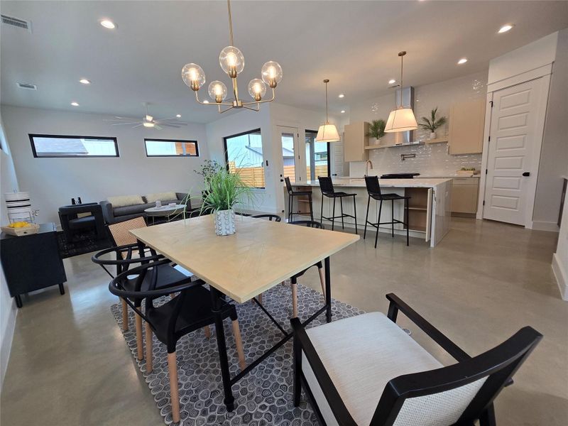 Dining area featuring ceiling fan with notable chandelier, visible vents, recessed lighting, and finished concrete flooring Dining area featuring ceiling fan with notable chandelier, visible vents, recessed lighting, and finished concrete flooring