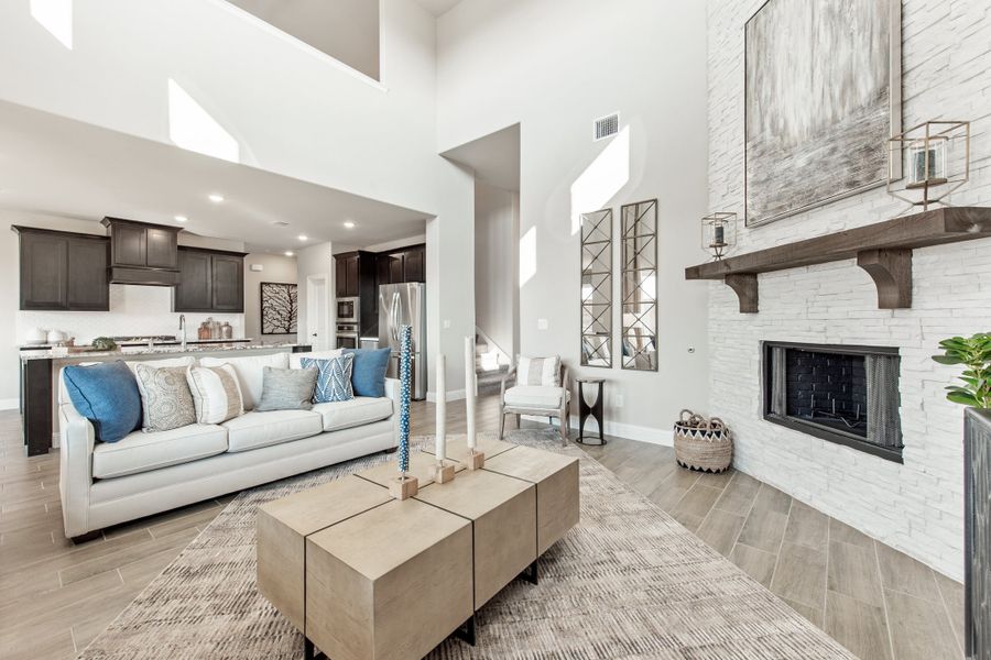 Open-concept living room with vaulted ceiling, white brick fireplace, and view into kitchen Open-concept living room with vaulted ceiling, white brick fireplace, and view into kitchen