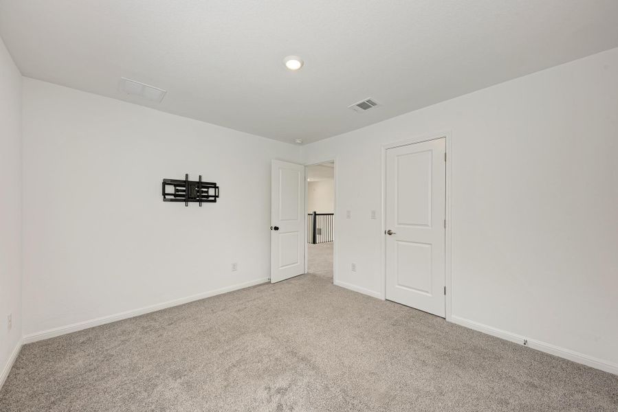A well-lit, neutral-toned room provides a versatile space, featuring plush carpet and crisp white doors.