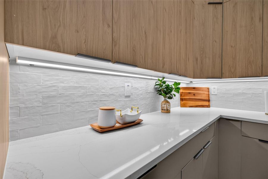 Sleek kitchen features modern wood cabinetry, elegant white countertops, and a stylish tile backsplash, creating a clean and inviting space.