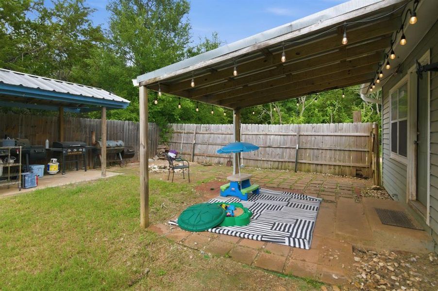 Spacious backyard featuring a covered patio with string lights, a secondary covered outdoor cooking area, a wood privacy fence, and a green lawn